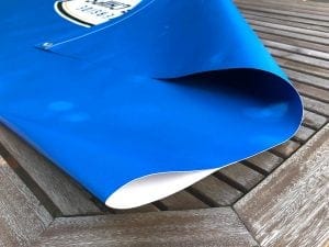 Close-up of a blue heavy-duty PVC banner with a curved edge, placed on a wooden table, showcasing its quality and suitability for outdoor cafe barrier systems.